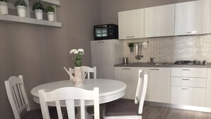 Une cuisine moderne avec des meubles blancs, une table de salle à manger ronde entourée de chaises blanches, et un four à micro-ondes placé au-dessus de la cuisinière.