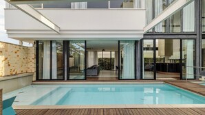 A modern house with a swimming pool, large glass doors, and a wooden deck.
