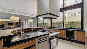 A modern kitchen with a central island, stainless steel appliances, and large windows offering views of the outdoors.