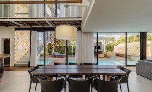 Un'area pranzo moderna con un tavolo grande e sedie, un lampadario e vista su una piscina e un'area relax esterna.