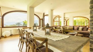 A dining area with a wooden table, chairs, and a view through large windows.