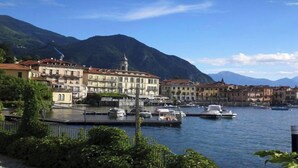 A waterfront town with buildings along the river, boats docked, and mountains in the background.