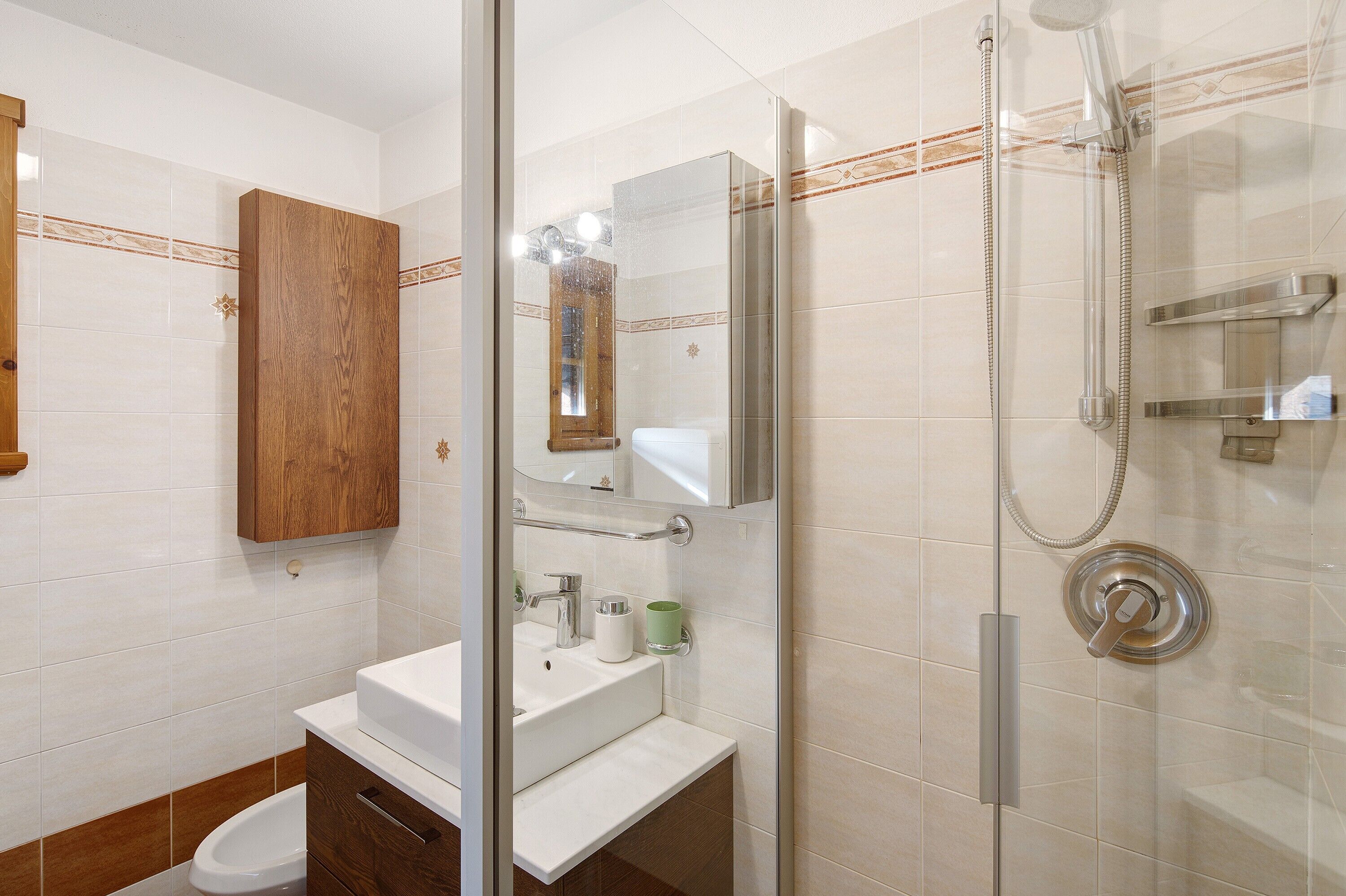 A bathroom with a glass shower enclosure, a wooden cabinet, and a white sink.