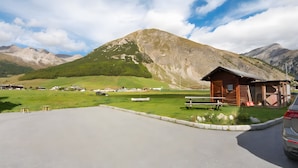 A mountain landscape with a wooden cabin, a paved parking area, and a clear sky. - Apartment 'Campacc Baby' with Mountain View, Shared Garden and Wi-Fi (Livigno)