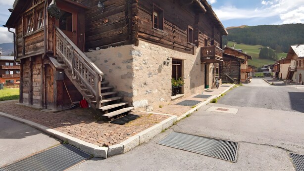 A rustic wooden building with a stone facade, a wooden staircase leading to the entrance, and a paved street in front. - Apartment 'Campacc Baby' with Mountain View, Shared Garden and Wi-Fi (Livigno)