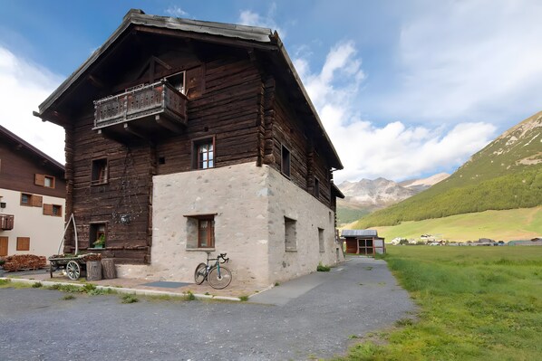 Un bâtiment rustique en bois, doté d’un balcon, avec un vélo et une charrette remplie de bois de chauffage.