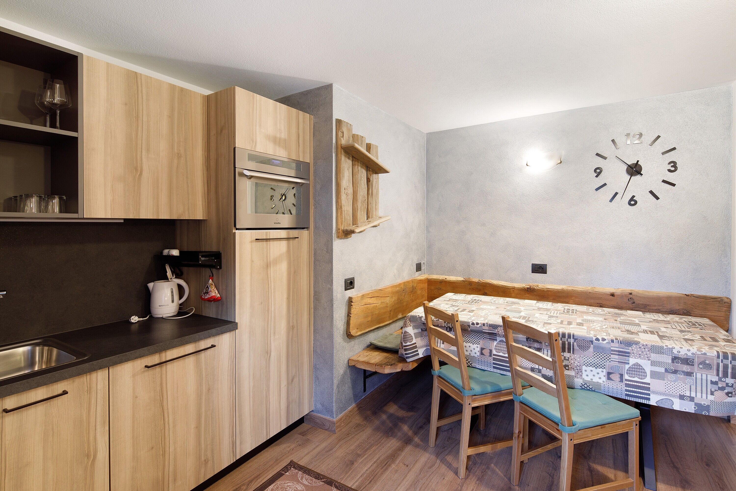 Een compacte keuken met houten kastjes, een ingebouwde oven, een spoelbak en een eethoek met een tafel en stoelen.
