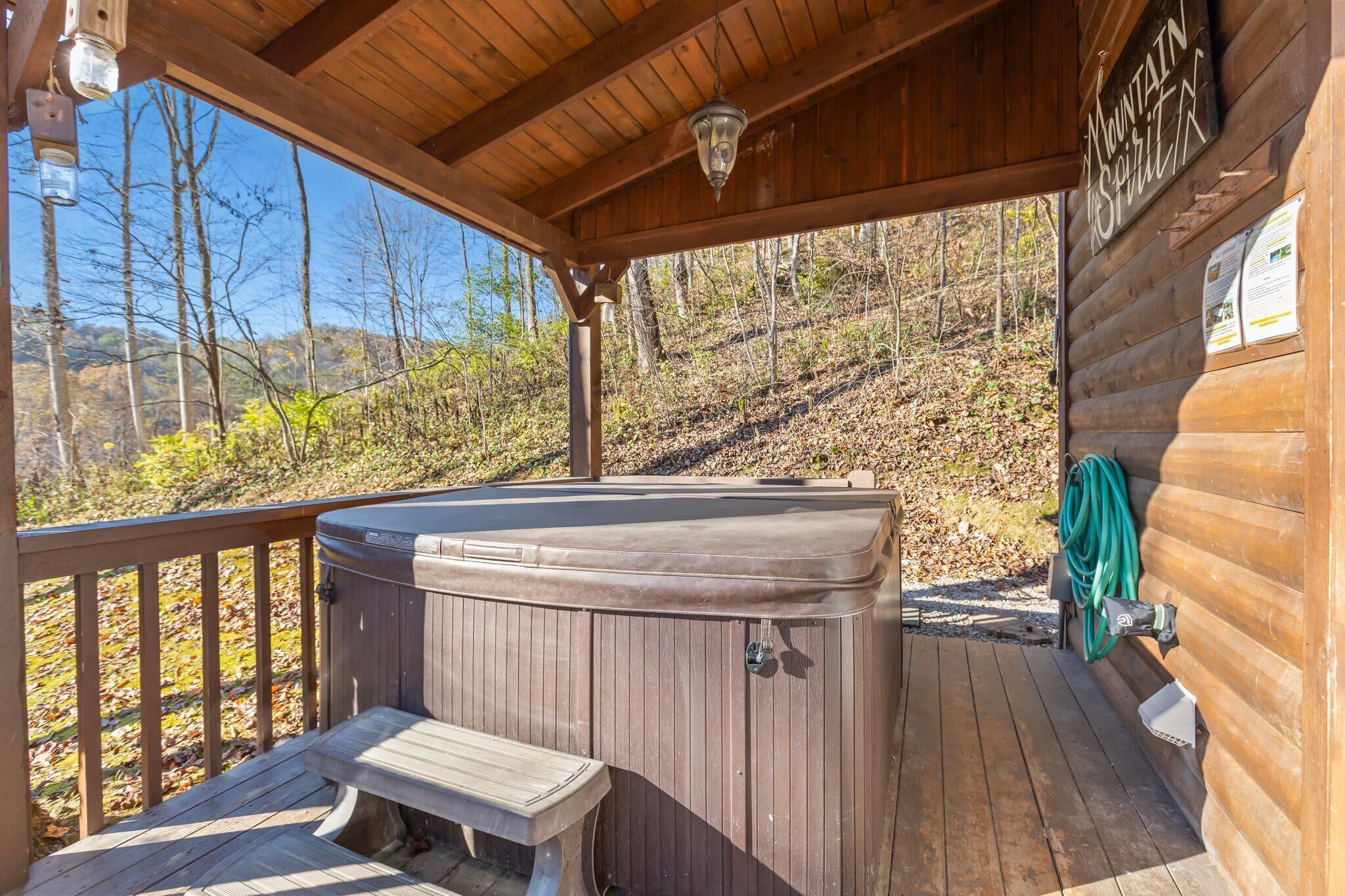 Um deck de madeira com uma banheira de hidromassagem, um banco e uma cabana de madeira com uma placa que diz 'Mountain Spirit'.