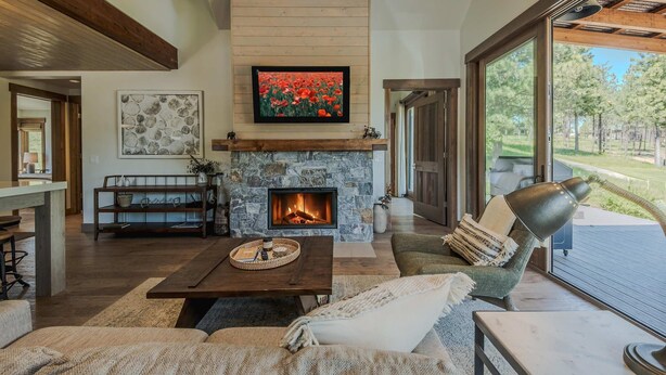 A cozy living room with a stone fireplace, a television mounted above it, and a comfortable seating area with a view of the outdoors. - Cottage on the 10th Tee Beautiful Stay for 7 w/ Hot Tub & Fire Pit (Eureka)