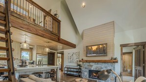 A spacious living area with a high ceiling, a fireplace, a dining area with a large island, and a cozy seating arrangement. - Cottage on the 10th Tee Beautiful Stay for 7 w/ Hot Tub & Fire Pit (Eureka)