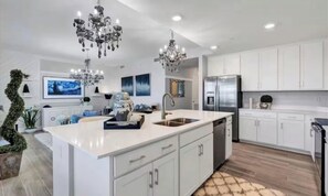 Une cuisine moderne avec des meubles blancs, un grand îlot central, des appareils électroménagers en acier inoxydable et un lustre.