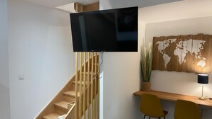 A modern living room with a wooden staircase, a flat-screen TV mounted above it, a desk with two chairs, and a world map wall art. - Love Room downtown with Jacuzzi (Bourges)