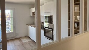 Uma cozinha moderna com armários brancos, forno embutido e janela com vista para uma varanda.