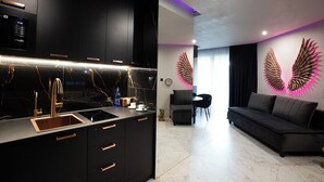 Eine moderne Küche mit schwarzen Schränken, einer Edelstahl-Arbeitsplatte und Kupfergriffen. Ein Essbereich mit einem dunklen Sofa und einer wandmontierten Leuchte.