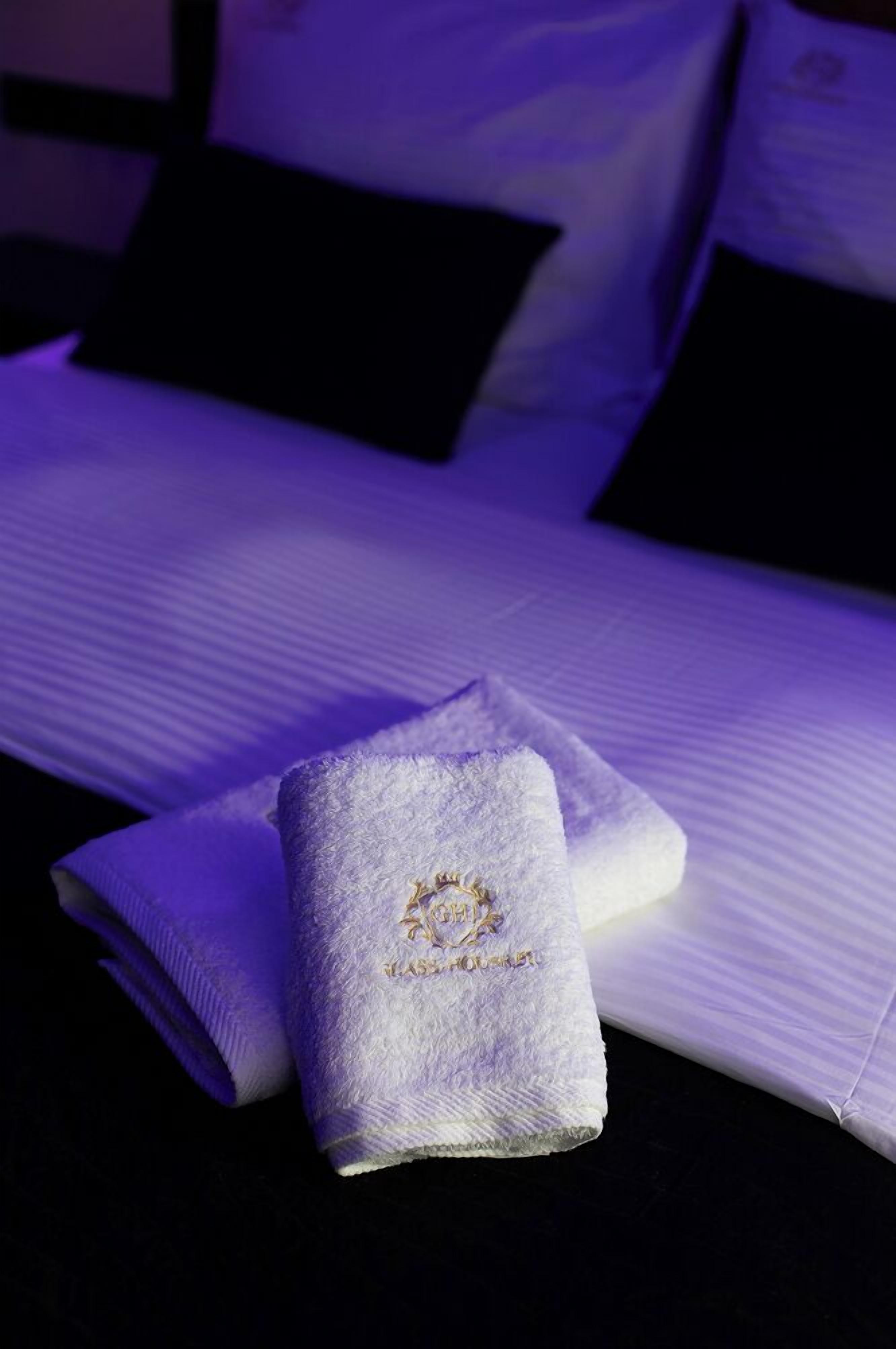 Una cama bien hecha con sábanas blancas y una toalla doblada con bordado.