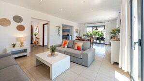 A modern living room with a grey sofa, white coffee table, and a dining area with a table and chairs.