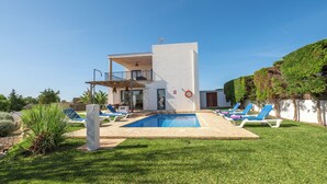 A modern two-story house with a swimming pool, sun loungers, and a well-maintained lawn.
