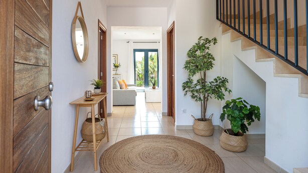 A modern interior with a wooden door, a round woven rug, a staircase with a metal railing, and potted plants.