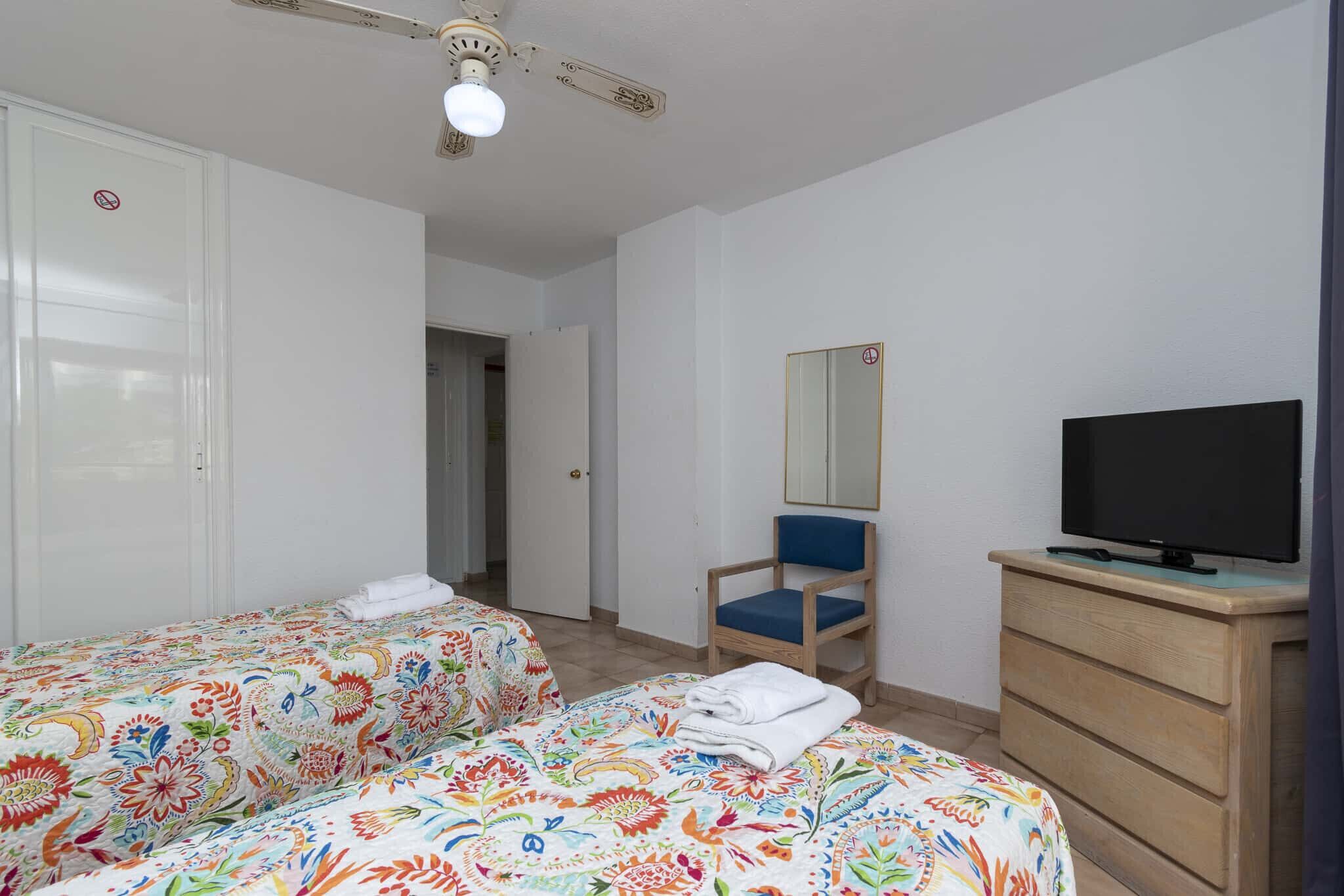 A bedroom with two beds, a chair, a dresser, a television, and a ceiling fan.