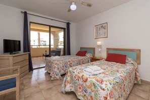 A hotel room with two beds, a TV, a desk, a chair, a balcony, and a ceiling fan.