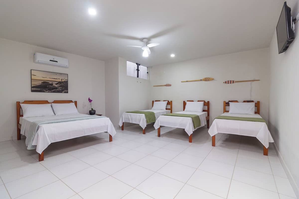 A hotel room with four single beds, a ceiling fan, an air conditioning unit, a painting, and a small potted plant.