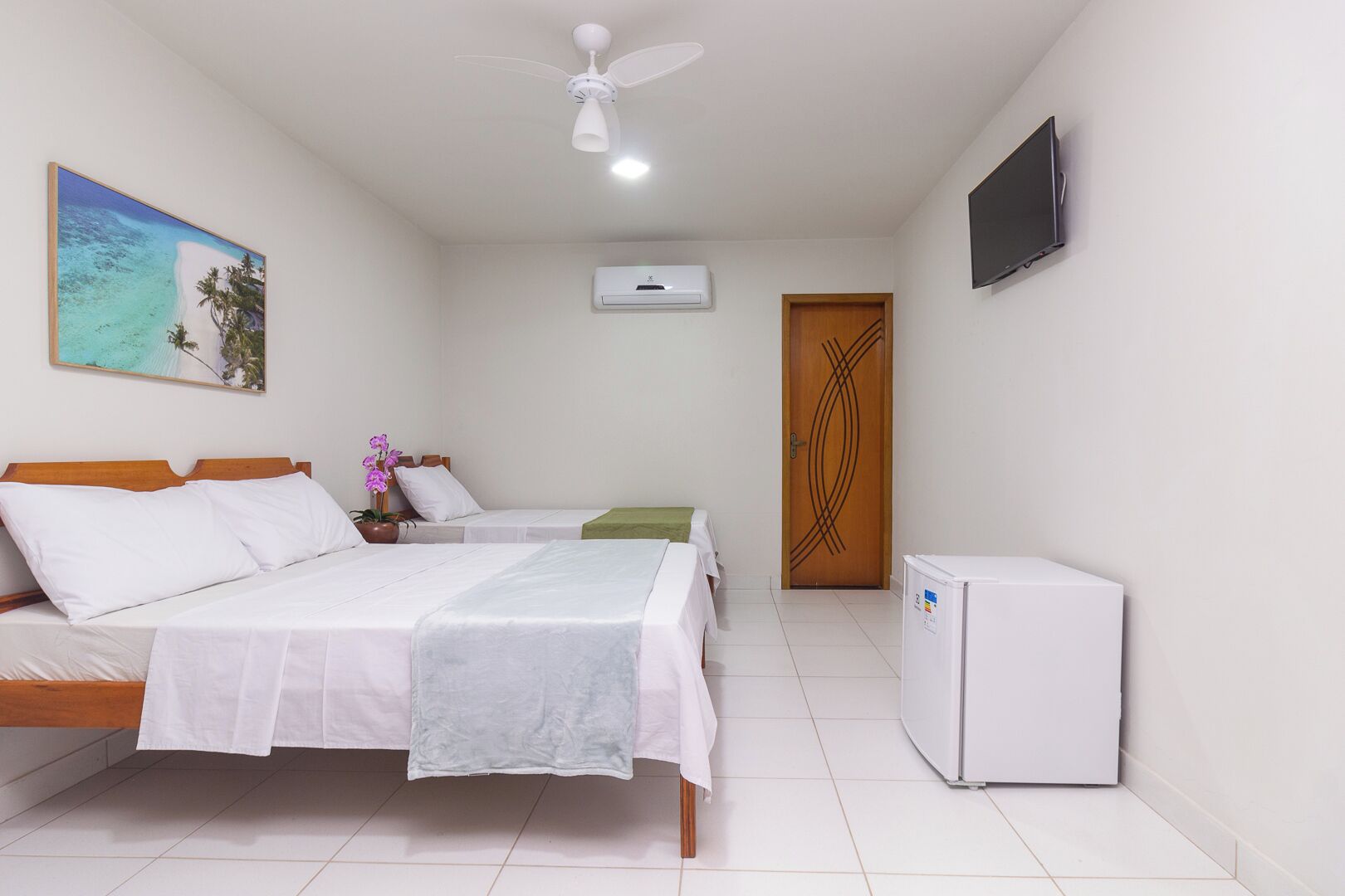 Una habitación de hotel con dos camas, ventilador de techo, aire acondicionado, televisor y refrigerador.