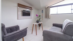A modern living room with two grey sofas, a flat-screen TV mounted on the wall, a small table with a potted plant, and a window with curtains. - Pousada Lagoa Azul (Paraty)