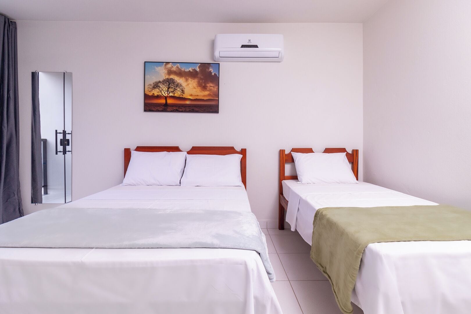 A hotel room with two beds, a painting of a tree, and an air conditioning unit.