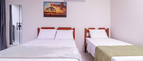 A hotel room with two beds, a painting of a tree, and an air conditioning unit.