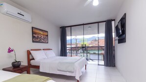 A hotel room with a bed, a small table with a plant, a painting, a TV, and a balcony with a view. - Pousada Lagoa Azul (Paraty)