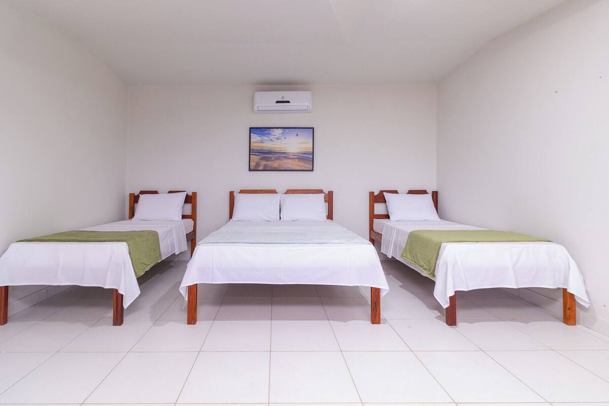 A room with three single beds, white bedding, and a painting on the wall.