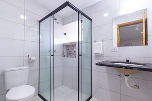 A modern bathroom with a glass-enclosed shower, a white toilet, a sink with a marble countertop, and a mirror with a wooden frame. - Pousada Lagoa Azul (Paraty)