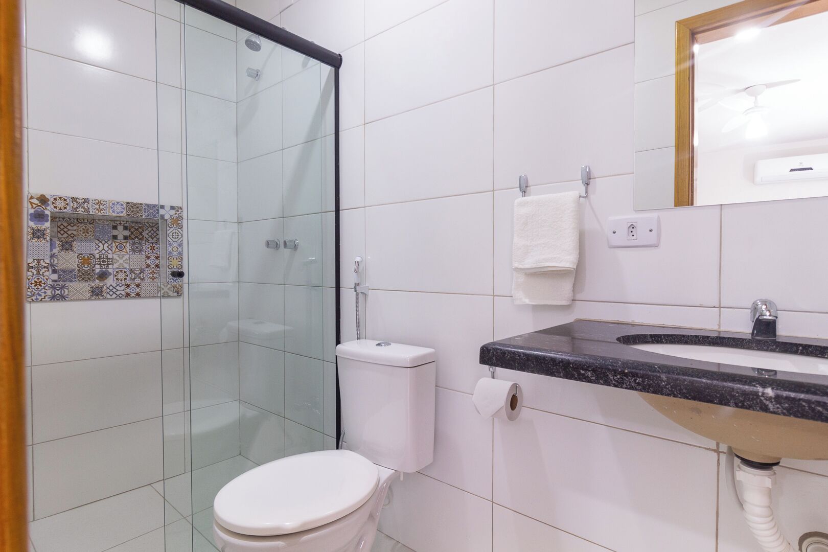 A bathroom with a glass-enclosed shower, a toilet, and a sink with a marble countertop.