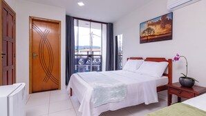 A hotel room with a bed, a nightstand, a window with curtains, a door, and a painting on the wall. - Pousada Lagoa Azul (Paraty)
