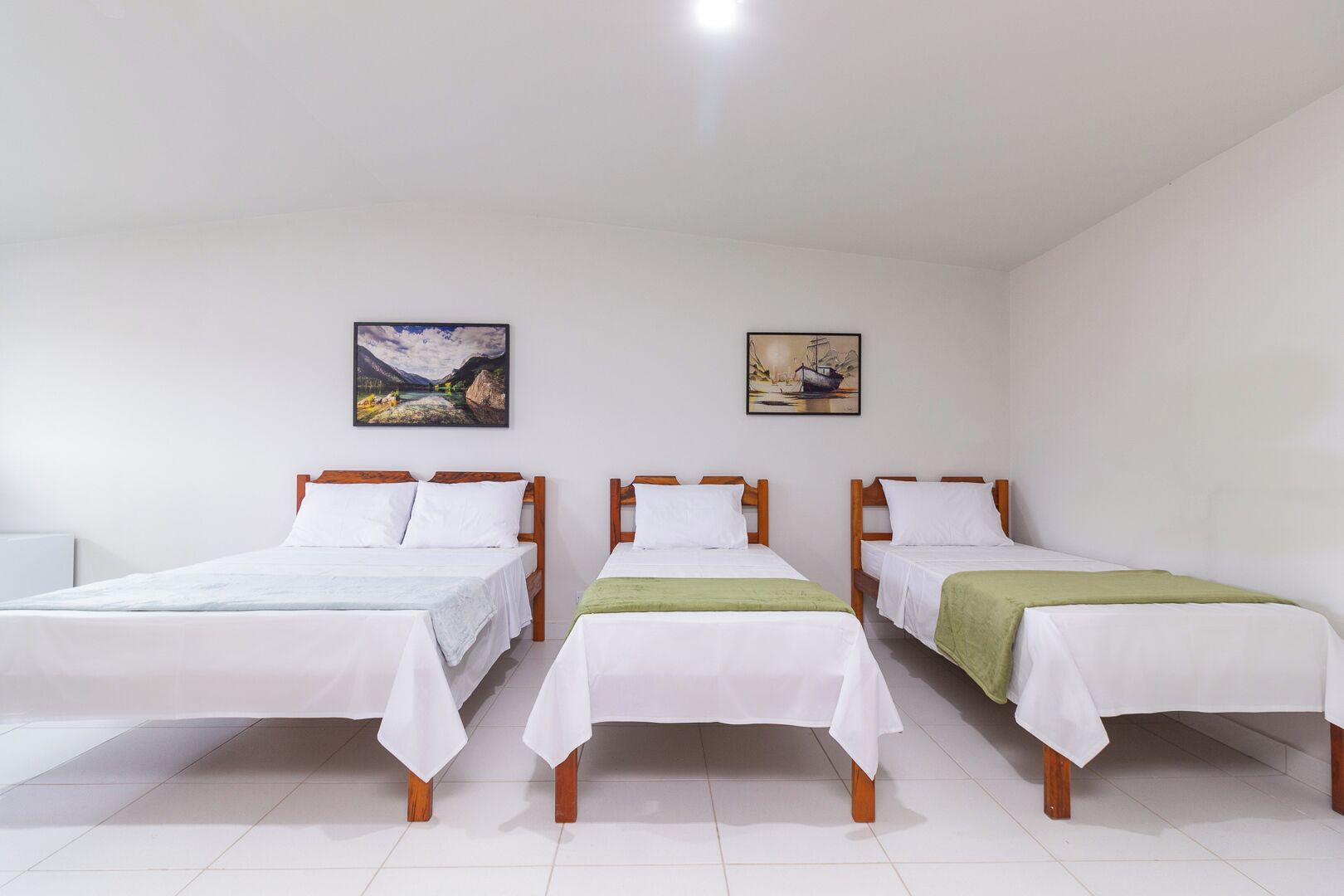 A hotel room with three single beds, white bedding, wooden headboards, and two wall-mounted paintings.