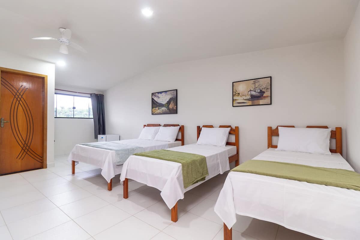 A hotel room with three single beds, a wooden door, a ceiling fan, and two paintings on the wall.