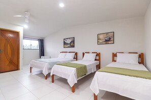 A hotel room with three single beds, a wooden door, a ceiling fan, and two paintings on the wall. - Pousada Lagoa Azul (Paraty)