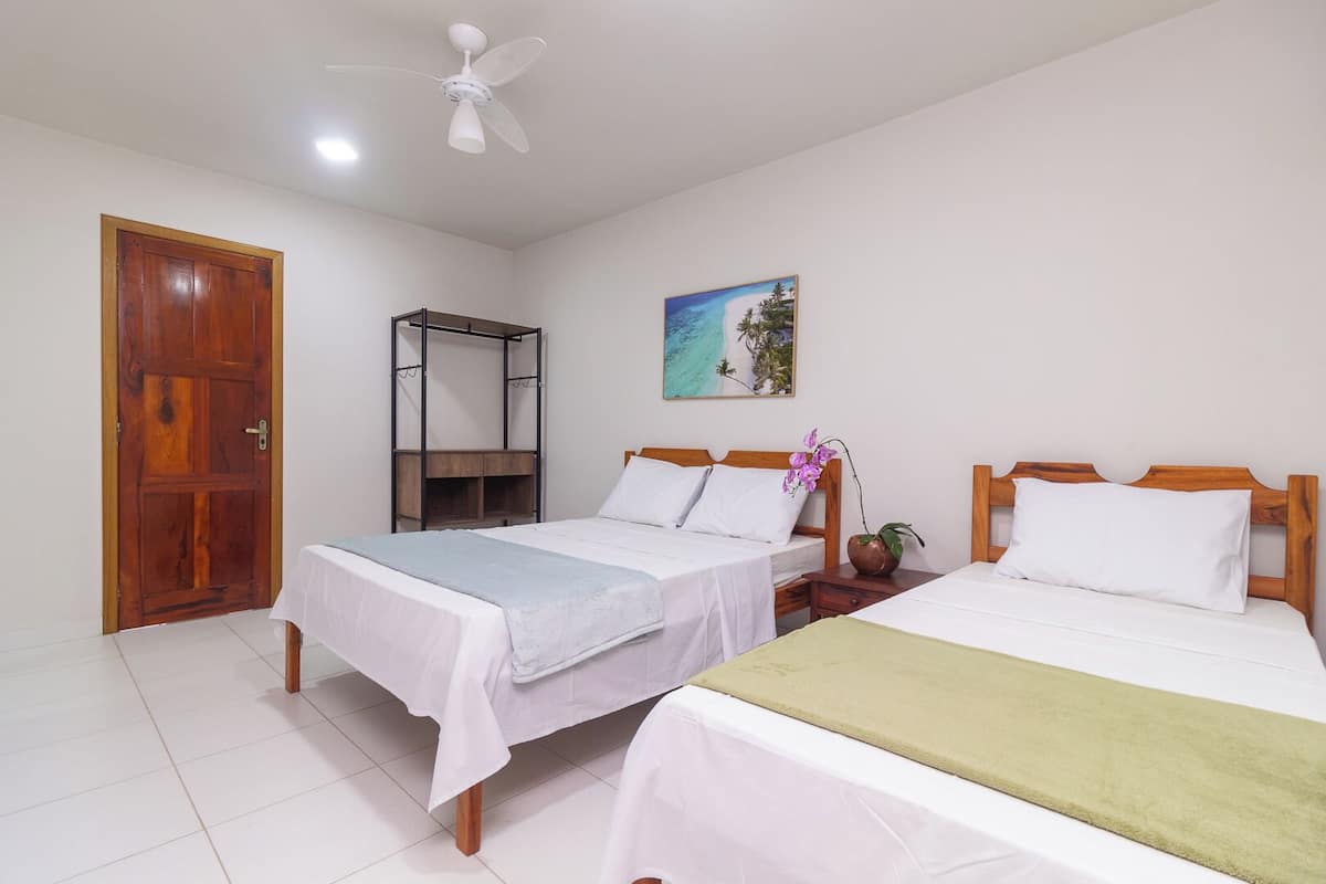 A room with two beds, a wooden door, a ceiling fan, and a painting on the wall.
