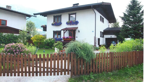 A two-story house with a wooden fence in front, a garden with various plants and flowers, and a clear view of the surrounding area.