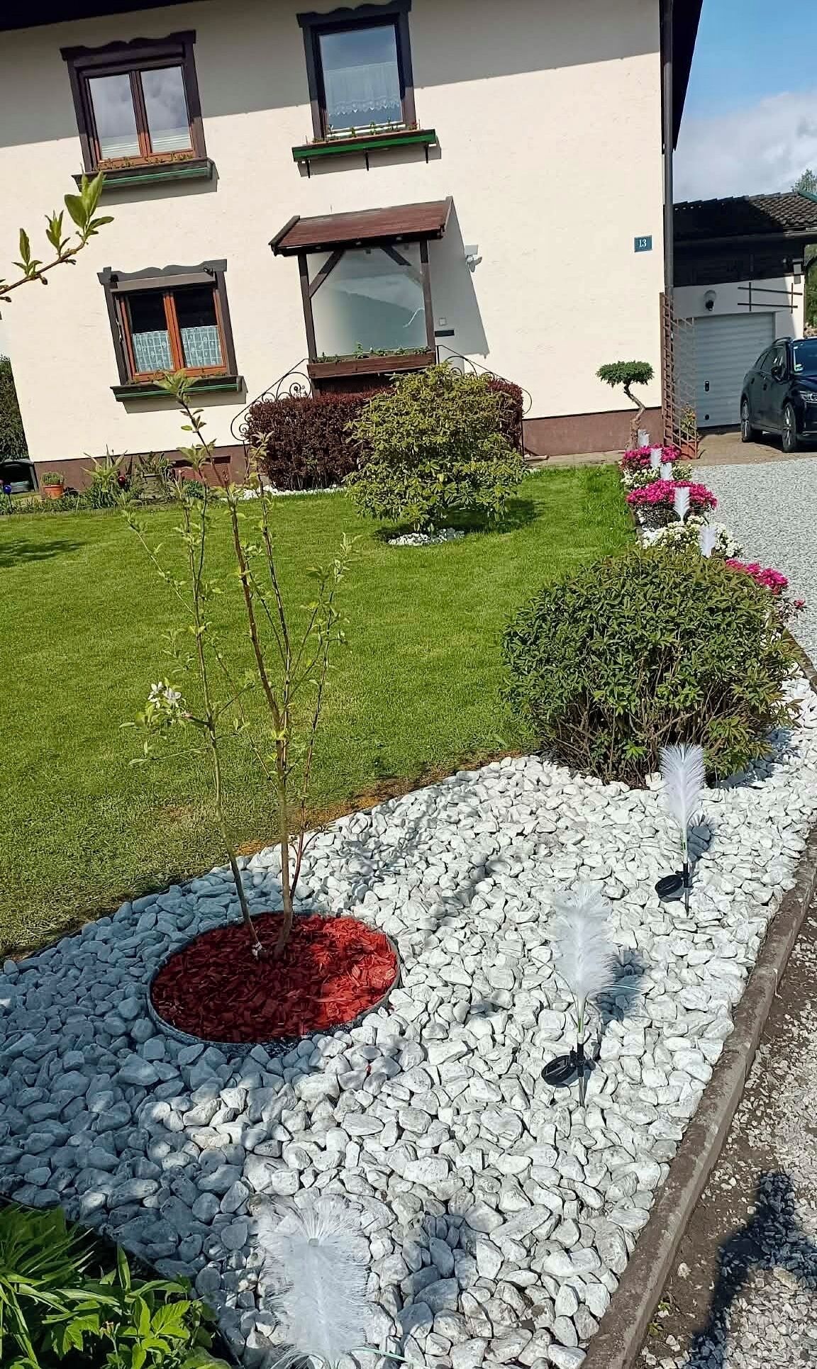 Ein Haus mit gepflegtem Rasen, einem kleinen Garten mit verschiedenen Pflanzen und einem Kiesweg.
