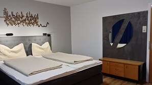 A bedroom with a bed, two pillows, a bedside table, a dresser, and a wall art piece.