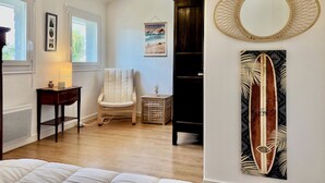 A room with a wooden floor, a white chair, a black bookshelf, a round mirror, and a framed picture on the wall. - Lec'h Mat-Port Haliguen Quiberon-Wifi-6p-linen included (Quiberon)