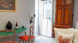 Ett rum med ett träskåp, ett grönt bord, en stol med en orangefärgad kudde och en vit soffa med ett kuddfodral i korallmönster.