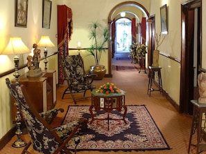 A hallway with a floral-patterned armchair, a small table with a flower arrangement, and a potted plant.