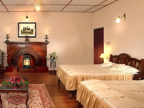 A hotel room with a fireplace, two beds, a wooden floor, and a dining table with a floral arrangement.