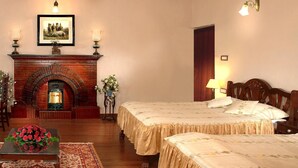 A hotel room with a fireplace, two beds, a wooden floor, and a dining table with a floral arrangement. - Welcomheritage Kasmanda Palace (Dehradun)