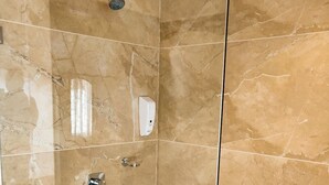 Una cabina doccia a filo pavimento con porta in vetro, pareti in marmo e soffione a mano.
