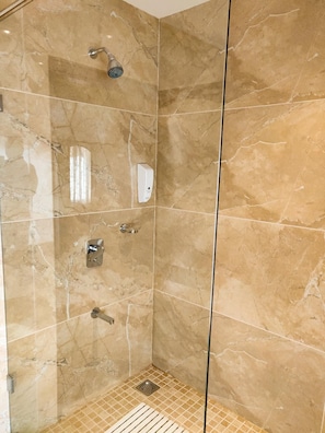 A walk-in shower with a glass door, marble walls, and a handheld showerhead.