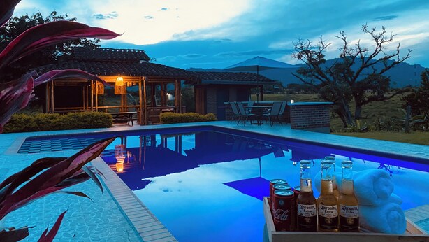 Un área de piscina con terraza de madera, sillas de descanso y una mesa con bebidas.