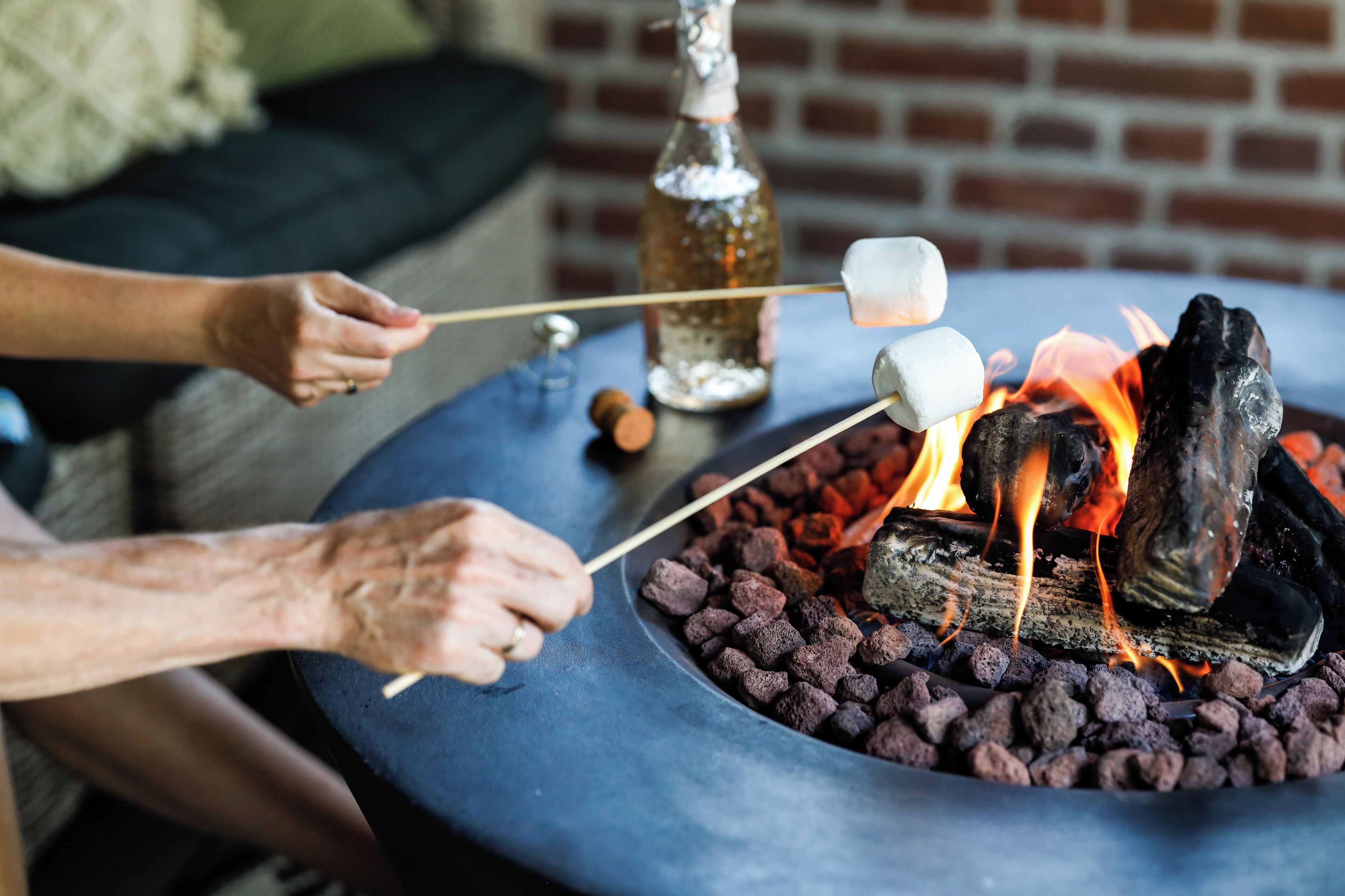 A person roasting marshmallows over a charcoal fire in a round outdoor grill.